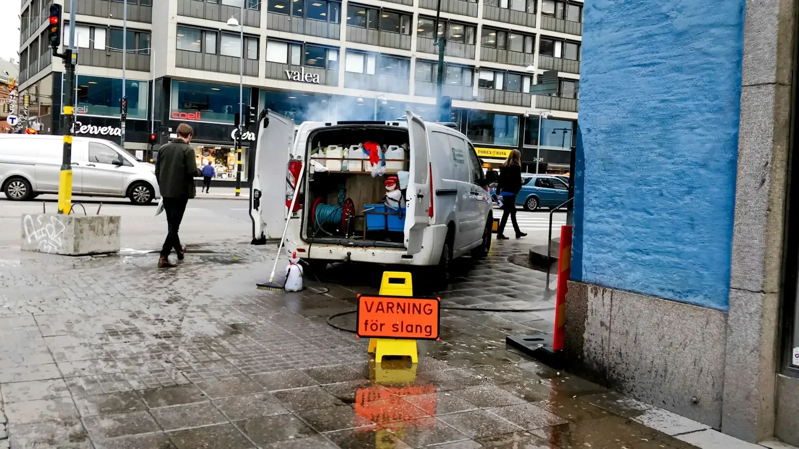 A service van with its rear doors open and a hose running onto a wet pavement